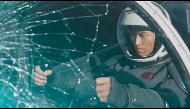 The same pilot, now in a white helmet and wearing the same round red chest badge, grips the controls behind a cockpit canopy cracked across its whole width